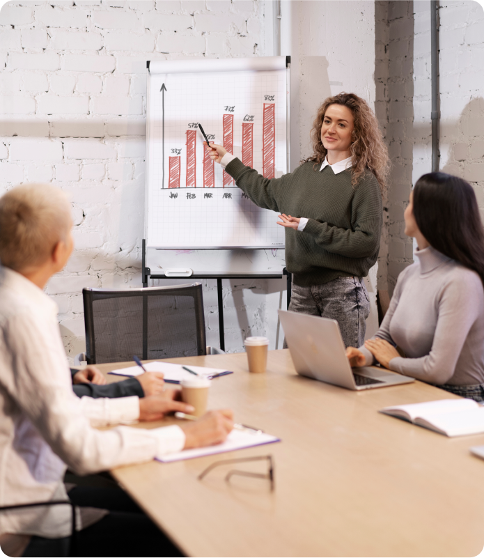 A woman, an eCommerce Team Lead, presents to a group of engaged colleagues in a conference room setting.