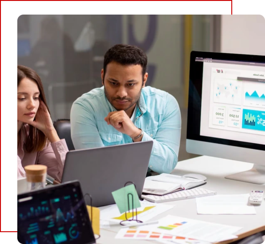 Two business professionals collaborate on Odoo implementation planning, positioned at a table with multiple screens displaying data visualizations. A woman with long brown hair appears to be in deep thought, while a man with light teal shirt rests his chin on his hand, showing concentration. A laptop, a tablet, and a desktop monitor are visible, along with documents containing graphs and charts scattered on the desk.