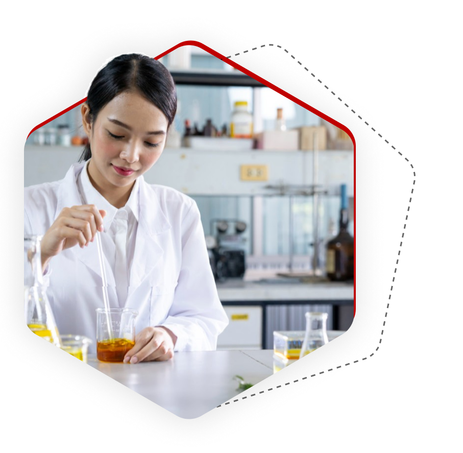 A woman in a white lab coat stands in a lab, concentrating as she stirs a yellow liquid in a beaker with a stirring rod. Several other beakers and lab equipment appear on the table in front of her. The background shows lab shelving and more scientific equipment. The scene is lit with cool, diffused light, typical of a laboratory setting.