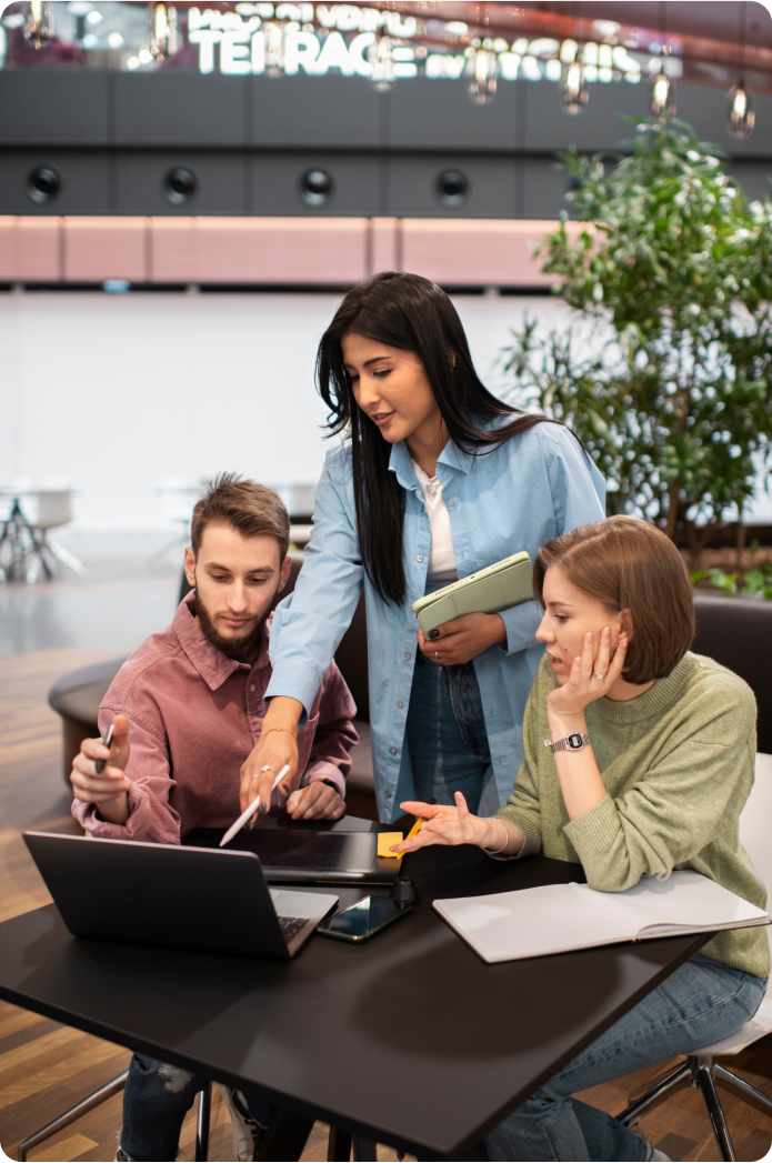 Three individuals engaged in a discussion while working on a laptop in an office, part of a manufacturing operations team.