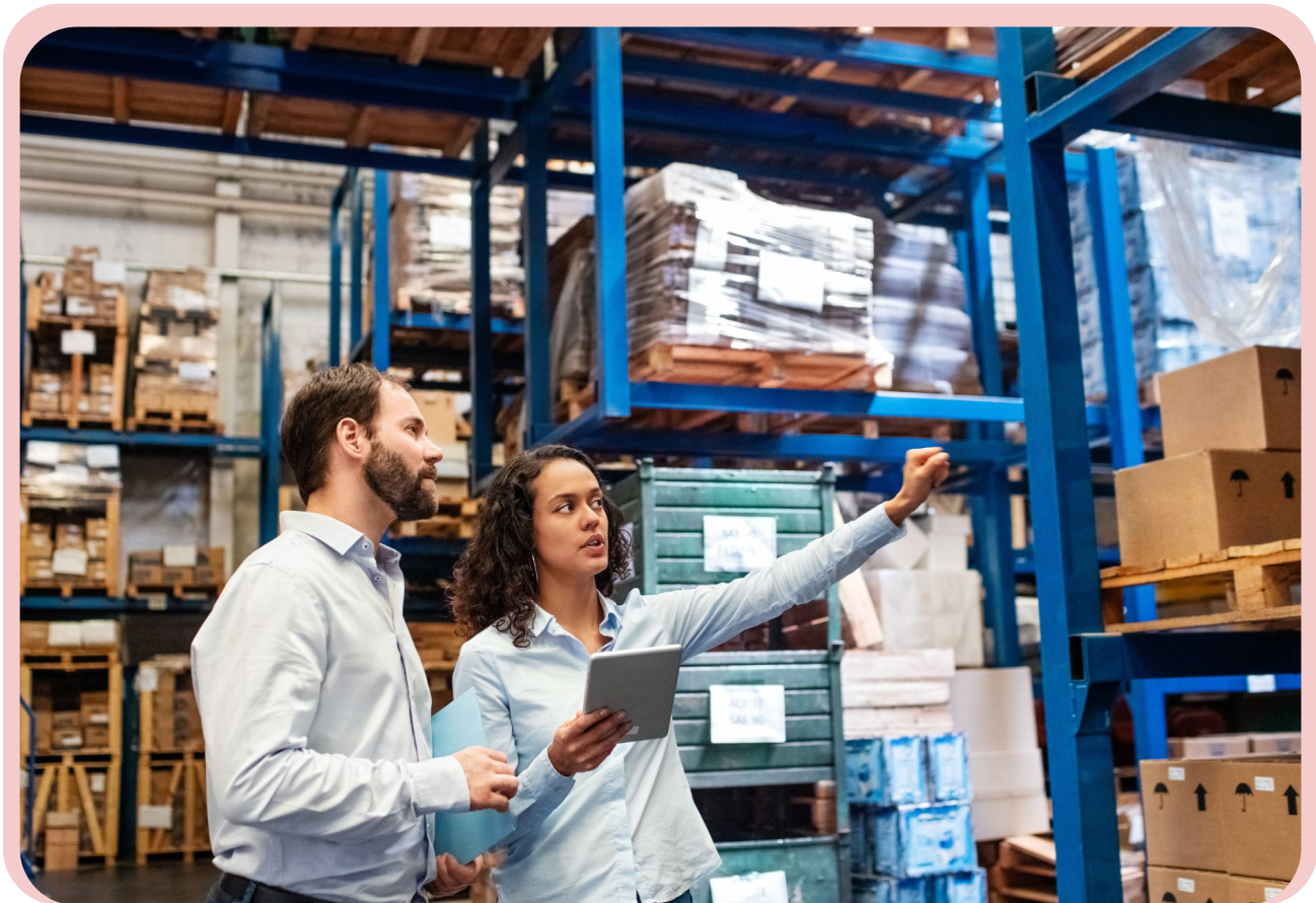 A man and a woman standing side by side in a warehouse environment, wearing work clothing.